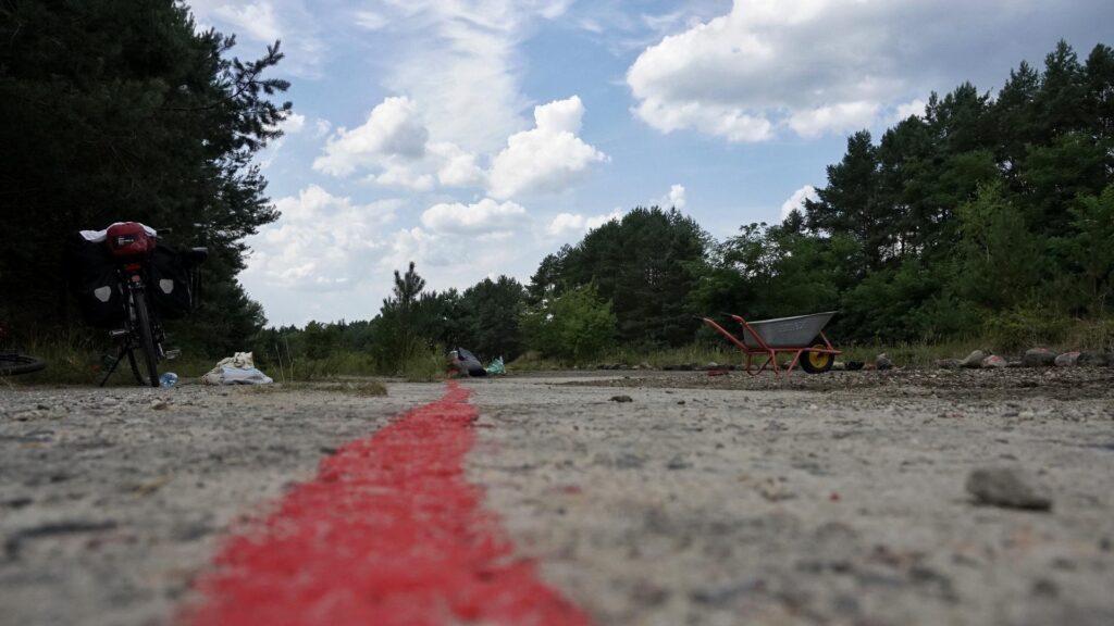 Ehemalige Lagerstraße des KZ Uckermark gekennzeichnet mit roter Farbe, im Hintergrund Schubkarre und andere Werkzeuge